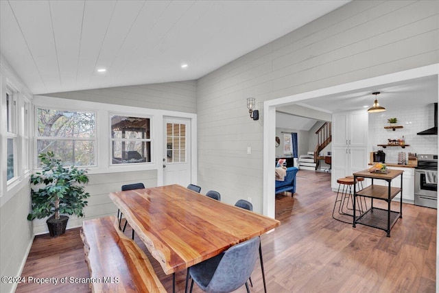 dining space featuring wooden walls, lofted ceiling, and light wood-type flooring