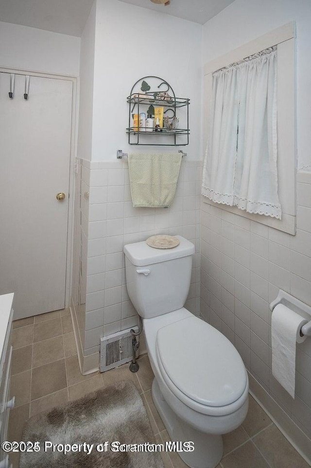 bathroom with tile patterned flooring, visible vents, toilet, and tile walls