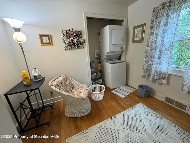 sitting room featuring wood finished floors, visible vents, stacked washer / drying machine, and baseboards