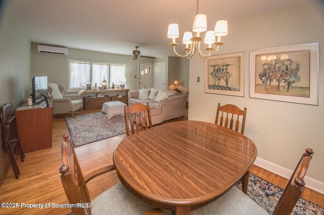dining space with light wood-type flooring, baseboards, an AC wall unit, and ceiling fan with notable chandelier