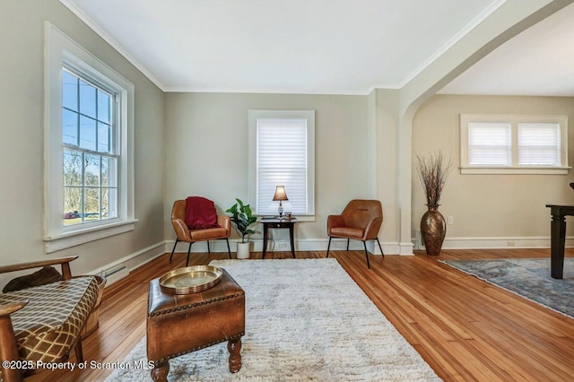 living area featuring baseboards, arched walkways, hardwood / wood-style flooring, baseboard heating, and crown molding