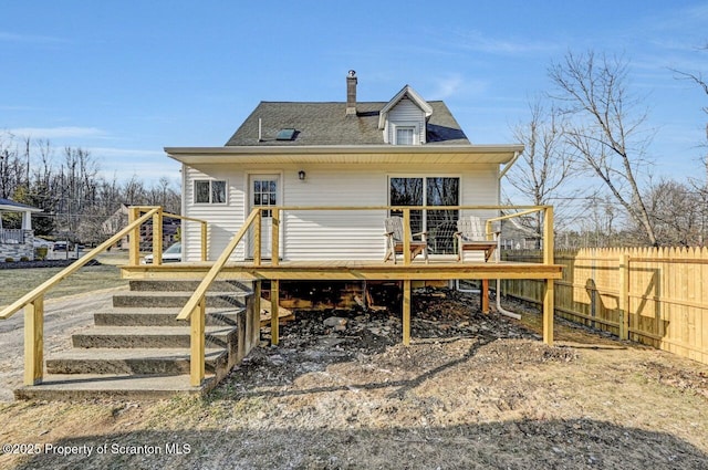 rear view of property featuring a shingled roof, fence, and a wooden deck