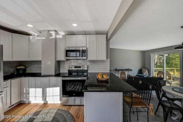 kitchen with stainless steel appliances, light wood-style floors, white cabinets, a peninsula, and a kitchen bar