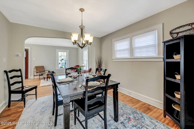 dining room featuring arched walkways, baseboards, light wood-style flooring, and a notable chandelier