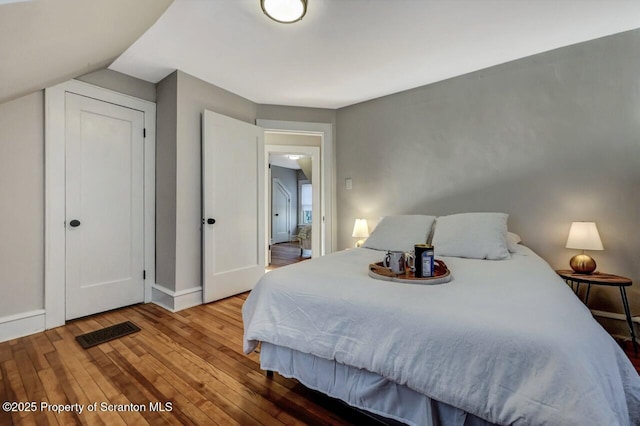 bedroom featuring lofted ceiling, hardwood / wood-style flooring, visible vents, and baseboards