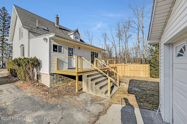 exterior space featuring roof with shingles, fence, a chimney, and a wooden deck