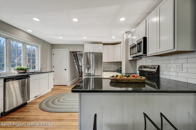 kitchen with light wood-style flooring, dark stone countertops, a peninsula, stainless steel appliances, and backsplash