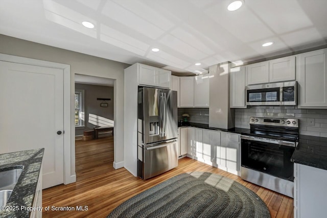 kitchen with recessed lighting, white cabinets, appliances with stainless steel finishes, light wood-type flooring, and backsplash