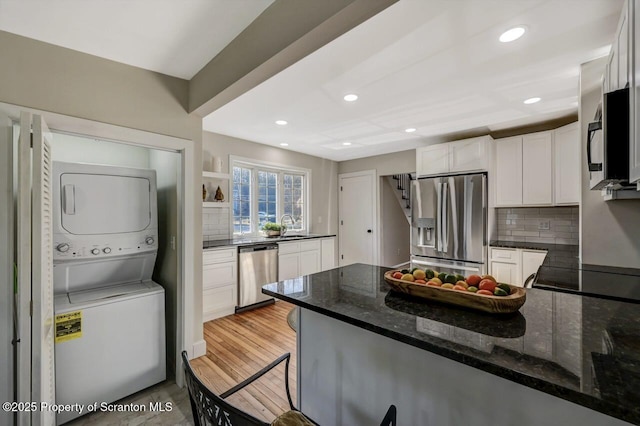 kitchen featuring stainless steel appliances, stacked washer and dryer, a peninsula, a sink, and white cabinets