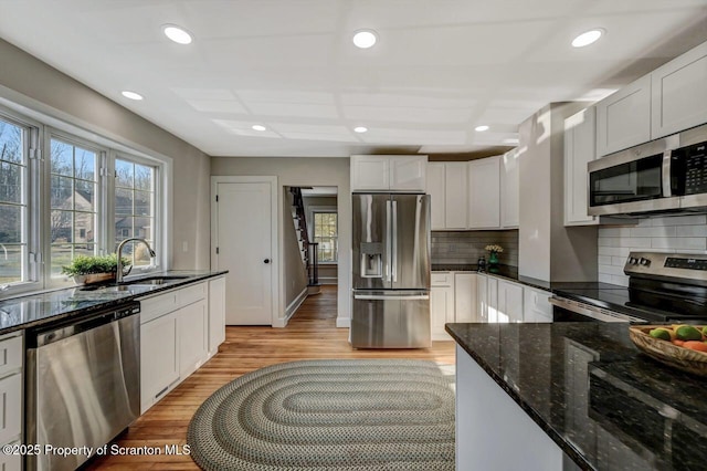 kitchen with tasteful backsplash, appliances with stainless steel finishes, a sink, dark stone countertops, and light wood-type flooring