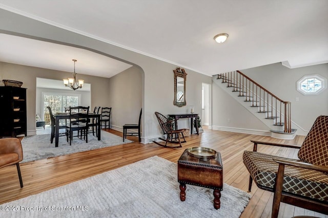 living area featuring light wood-style flooring, stairs, arched walkways, and baseboards