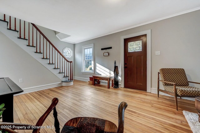 foyer featuring light wood-type flooring, baseboards, stairway, and crown molding