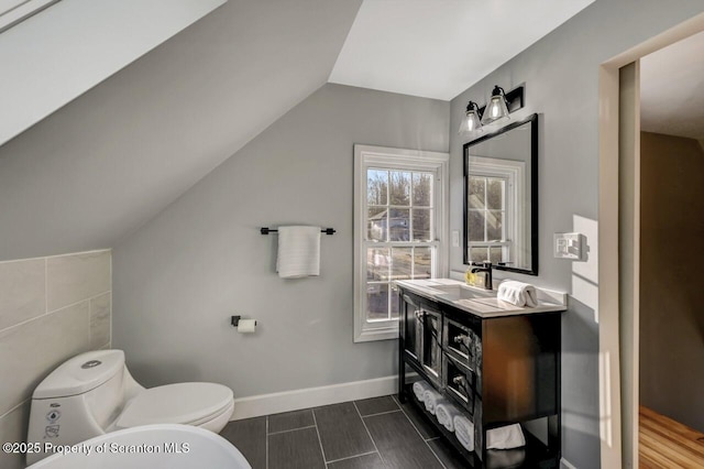 bathroom with baseboards, vaulted ceiling, vanity, and toilet