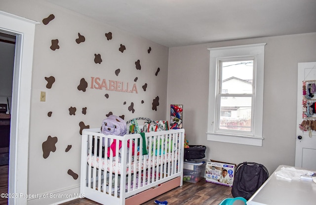 bedroom featuring baseboards, a crib, and wood finished floors