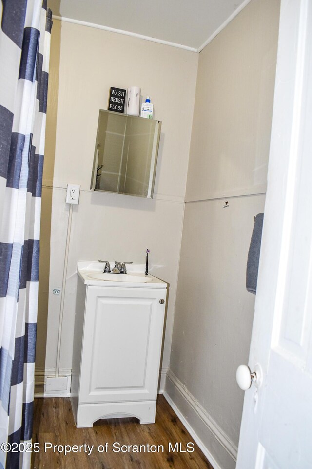bathroom featuring baseboards, ornamental molding, wood finished floors, and vanity