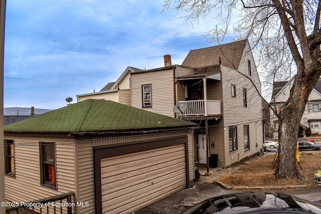 view of front of property featuring an attached garage, roof with shingles, a balcony, and a chimney