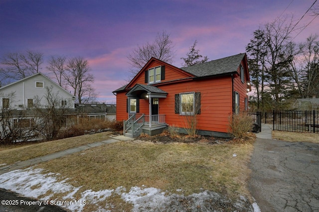 bungalow-style house with a shingled roof, fence, and a front lawn