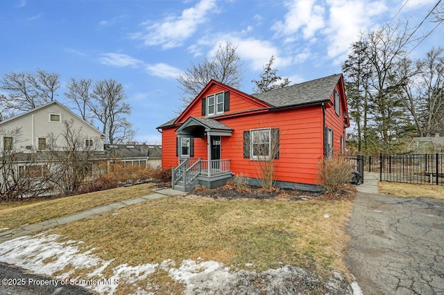 bungalow-style home with a shingled roof, fence, and a front yard