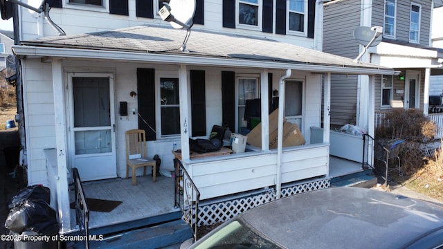 doorway to property featuring covered porch and roof with shingles