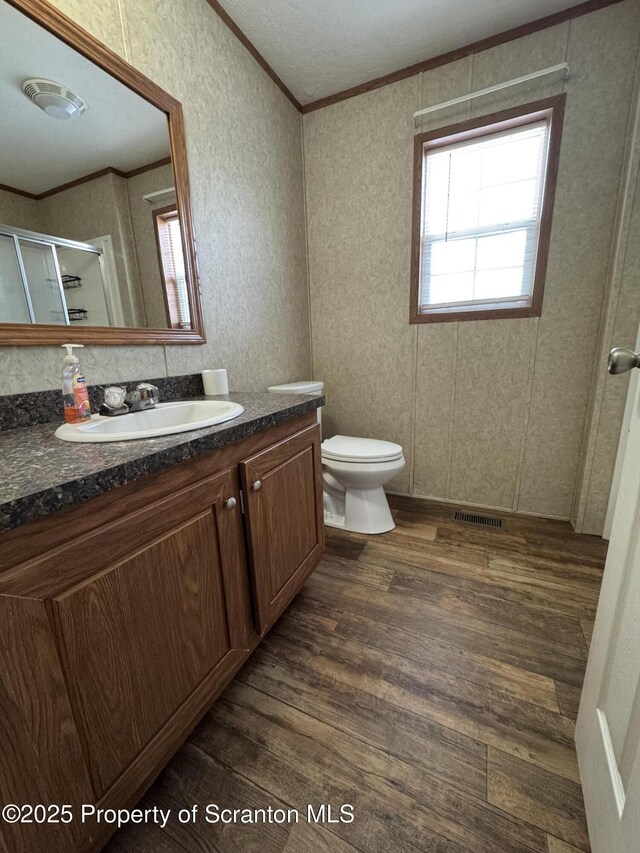 bathroom with walk in shower, crown molding, hardwood / wood-style floors, toilet, and vanity