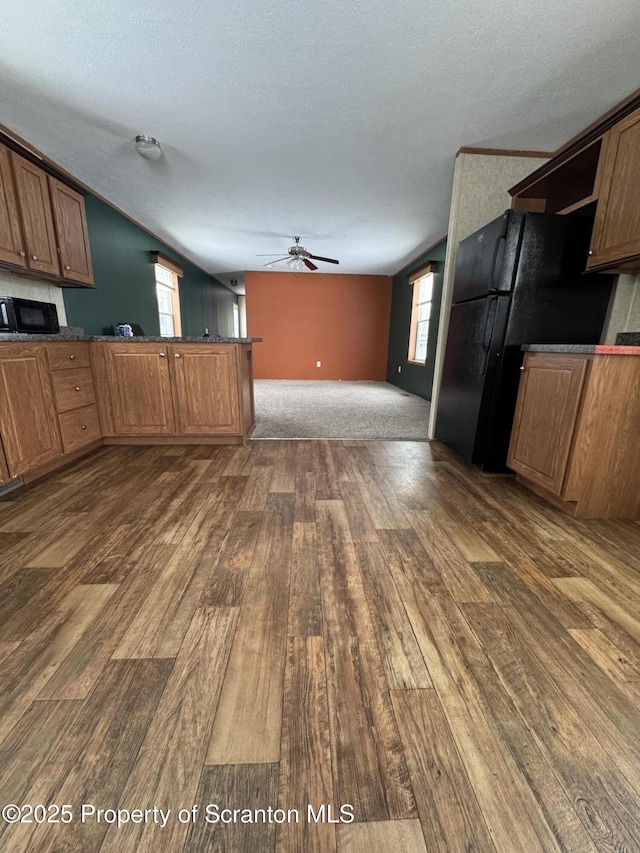 kitchen with dark wood-type flooring, black fridge, ceiling fan, a textured ceiling, and kitchen peninsula