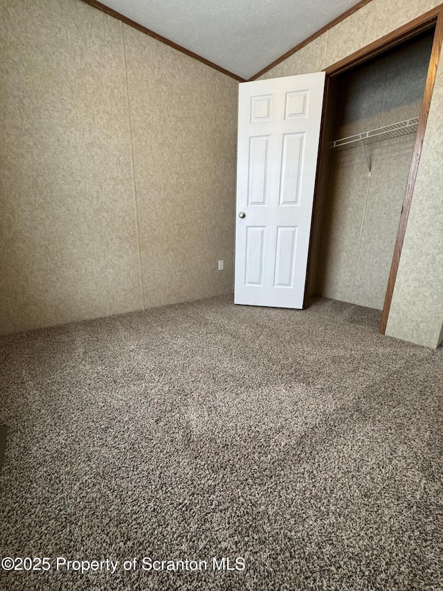 unfurnished bedroom featuring ornamental molding, a textured ceiling, vaulted ceiling, carpet floors, and a closet