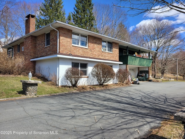 view of front of home featuring a balcony, a garage, brick siding, a chimney, and driveway