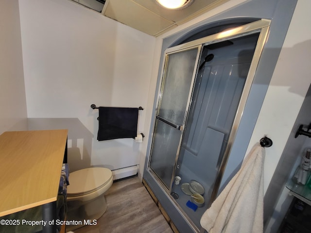 bathroom featuring toilet, a shower with shower door, wood finished floors, and a baseboard heating unit