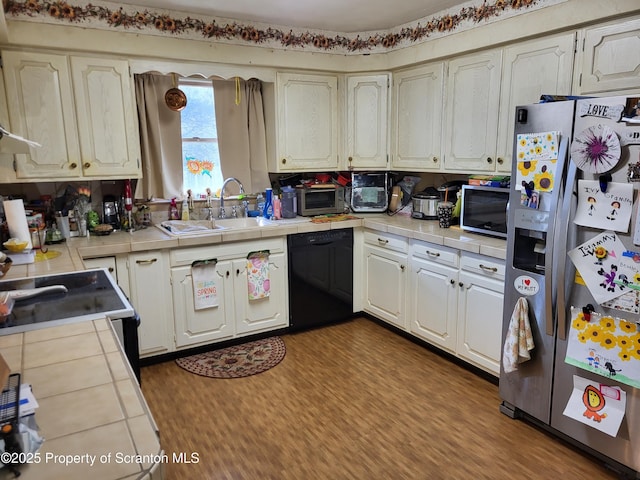 kitchen featuring a sink, appliances with stainless steel finishes, dark wood-style floors, tile counters, and white cabinetry
