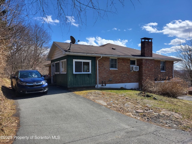 view of side of property featuring a chimney, cooling unit, board and batten siding, aphalt driveway, and brick siding
