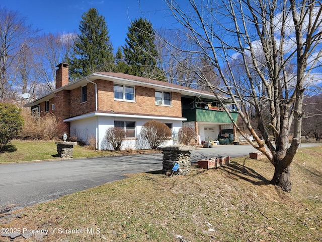 view of front of property featuring brick siding, aphalt driveway, and a chimney