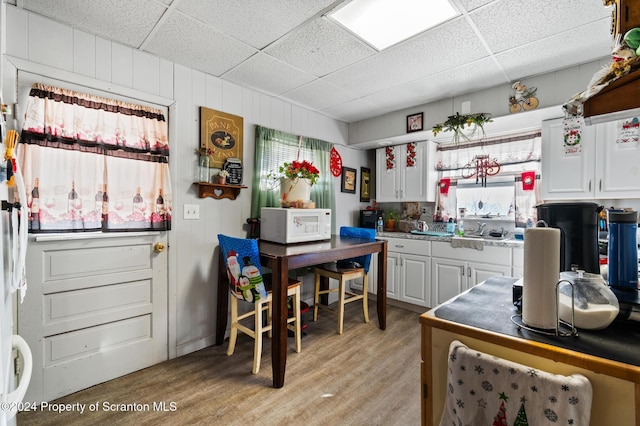 kitchen with white cabinets, a drop ceiling, light hardwood / wood-style floors, and sink