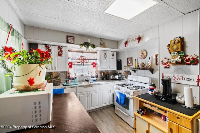 kitchen with white cabinetry, white gas stove, a drop ceiling, and light wood-type flooring