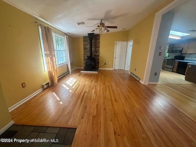 unfurnished living room with light hardwood / wood-style floors, lofted ceiling, a wood stove, and a baseboard heating unit