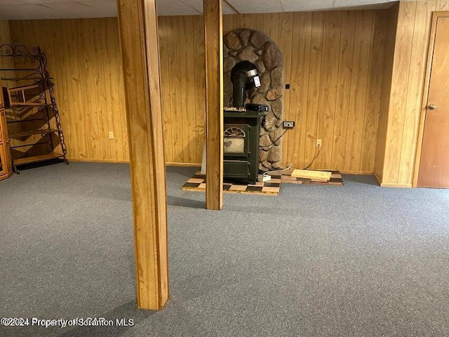 basement with carpet floors, a wood stove, a drop ceiling, and wooden walls