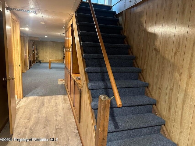 stairway featuring a paneled ceiling, wood walls, and hardwood / wood-style flooring