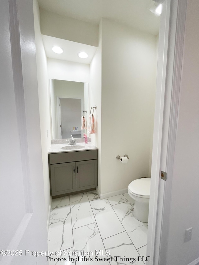 half bathroom with vanity, recessed lighting, toilet, marble finish floor, and baseboards