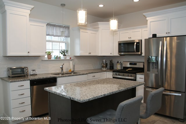 kitchen featuring white cabinetry, backsplash, a kitchen bar, stainless steel appliances, and a sink