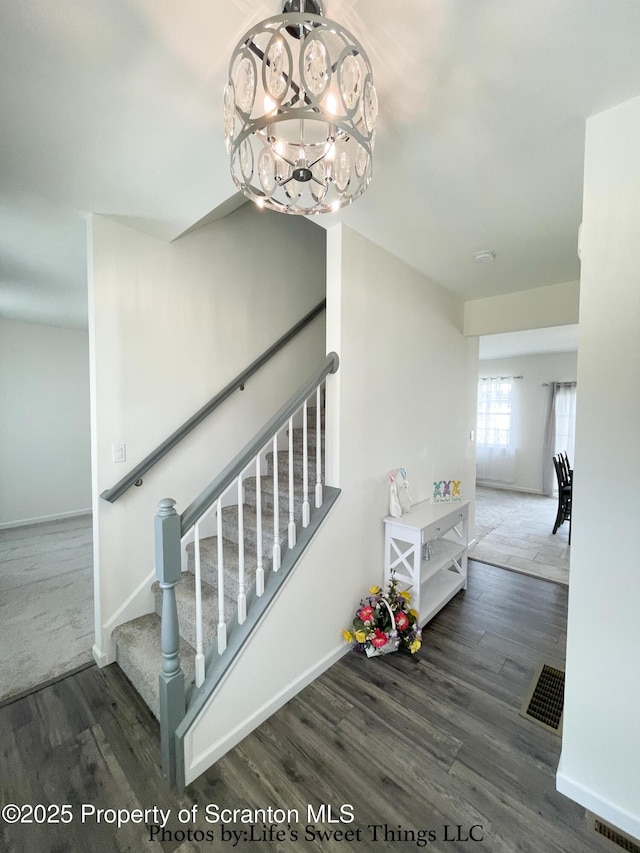 stairs featuring a chandelier, visible vents, baseboards, and wood finished floors