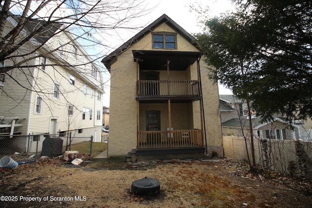 back of property with a balcony, fence, covered porch, and stucco siding