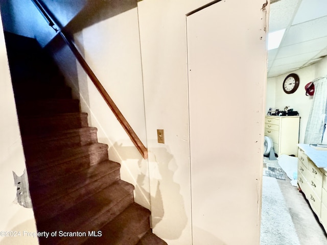 staircase featuring a paneled ceiling and concrete floors