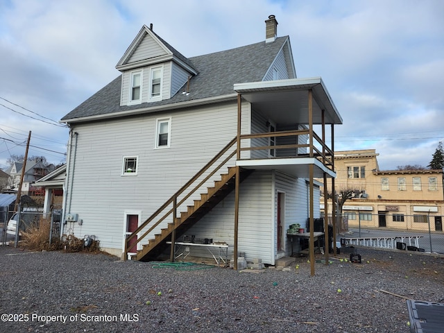 back of house featuring a chimney, stairway, a shingled roof, and fence