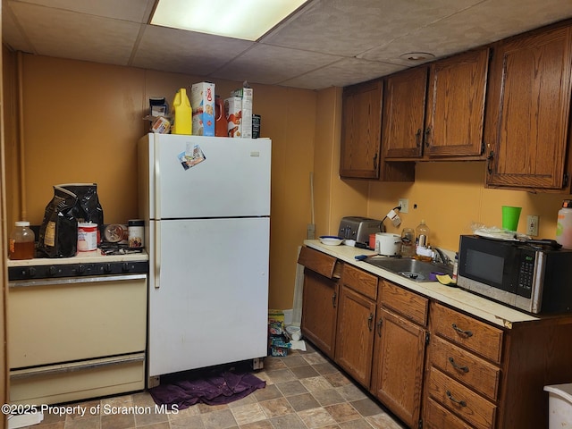 kitchen with brown cabinetry, white appliances, light countertops, and a sink