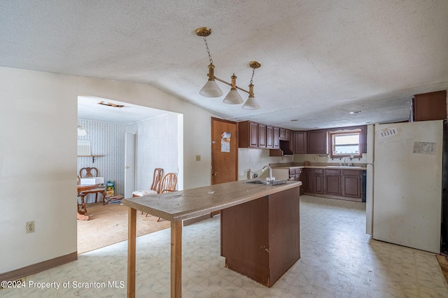 kitchen with sink, white fridge, hanging light fixtures, and lofted ceiling