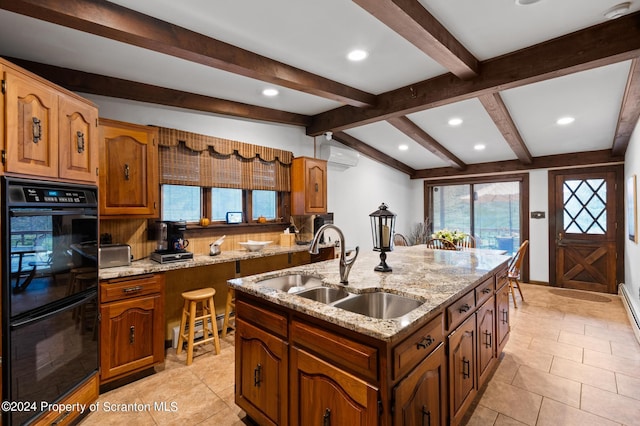 kitchen with a wall mounted air conditioner, a kitchen island with sink, sink, black double oven, and light stone counters