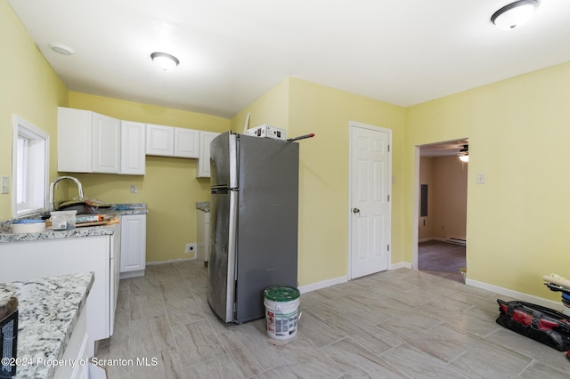 kitchen featuring white cabinets, stainless steel fridge, light stone countertops, and sink