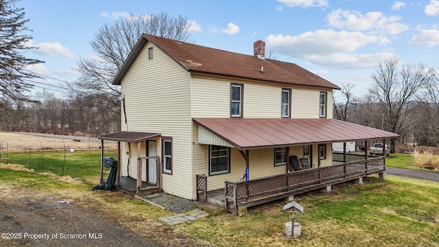 view of front of home featuring covered porch, a chimney, and a front lawn