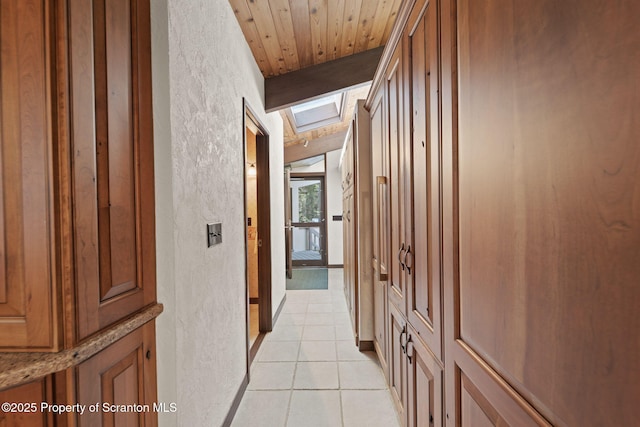 hall featuring a textured wall, a skylight, and light tile patterned floors