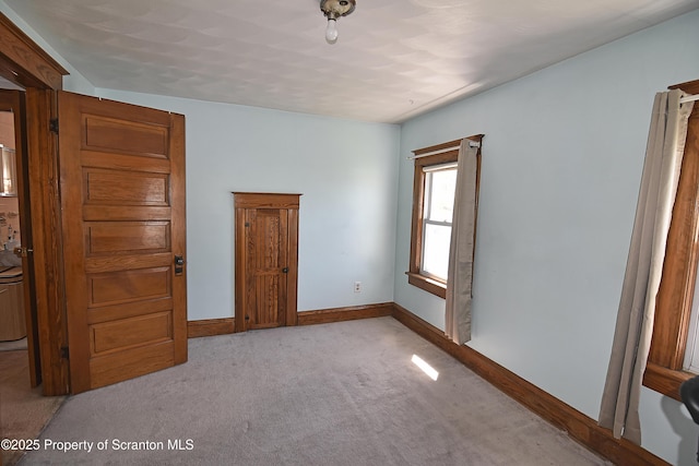 empty room featuring baseboards and light carpet