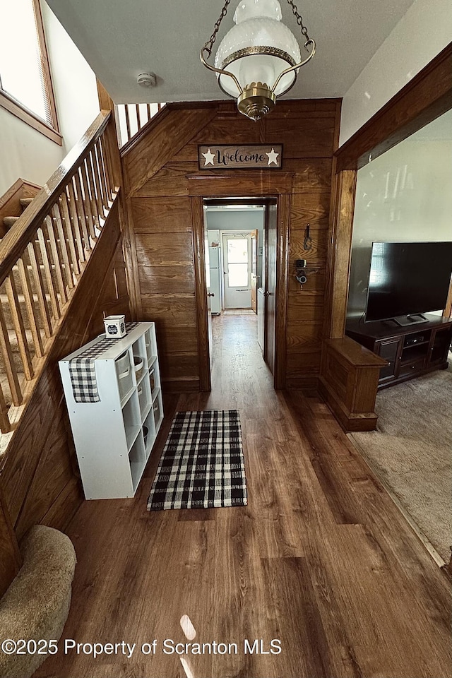 corridor with wood finished floors, wooden walls, and stairway